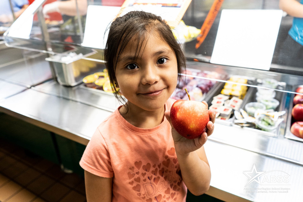 Student holding red apple in cafeteria line