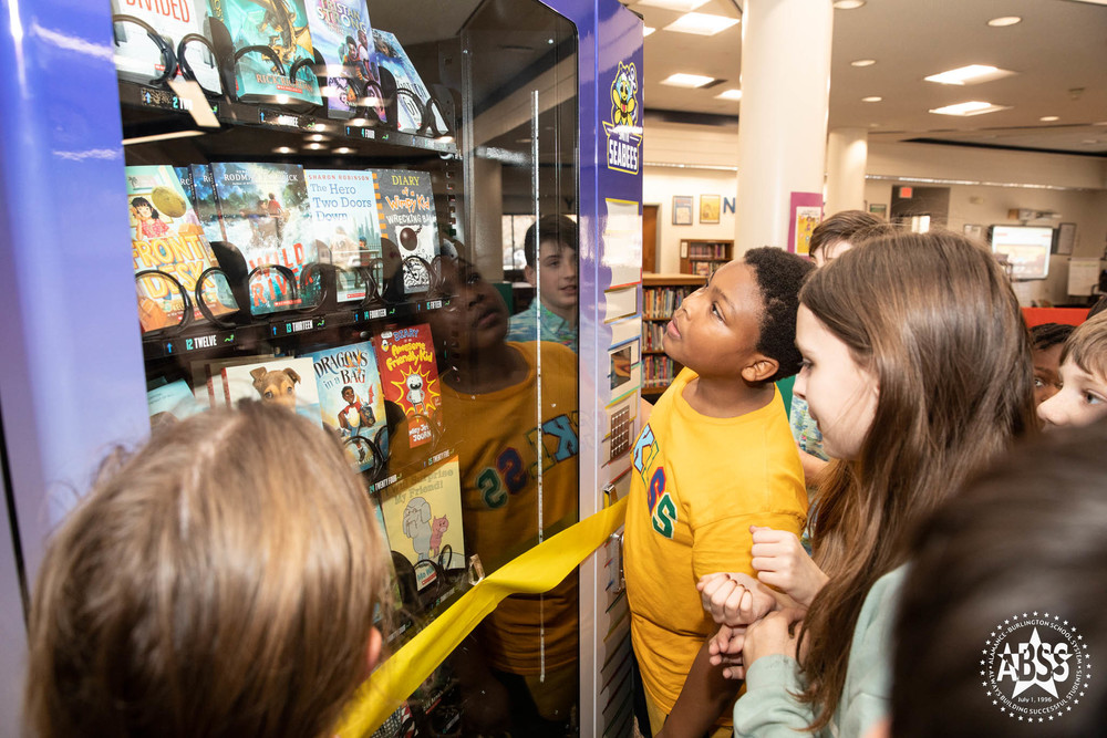 Students at Smith Elementary gathered around book vending machine smiling at the machine. 