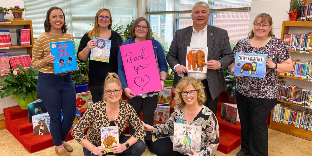 Six representatives from Edward Jones Financial Services and the librarian of Grove Park Elementary holding donated books and a large thank you card made by students