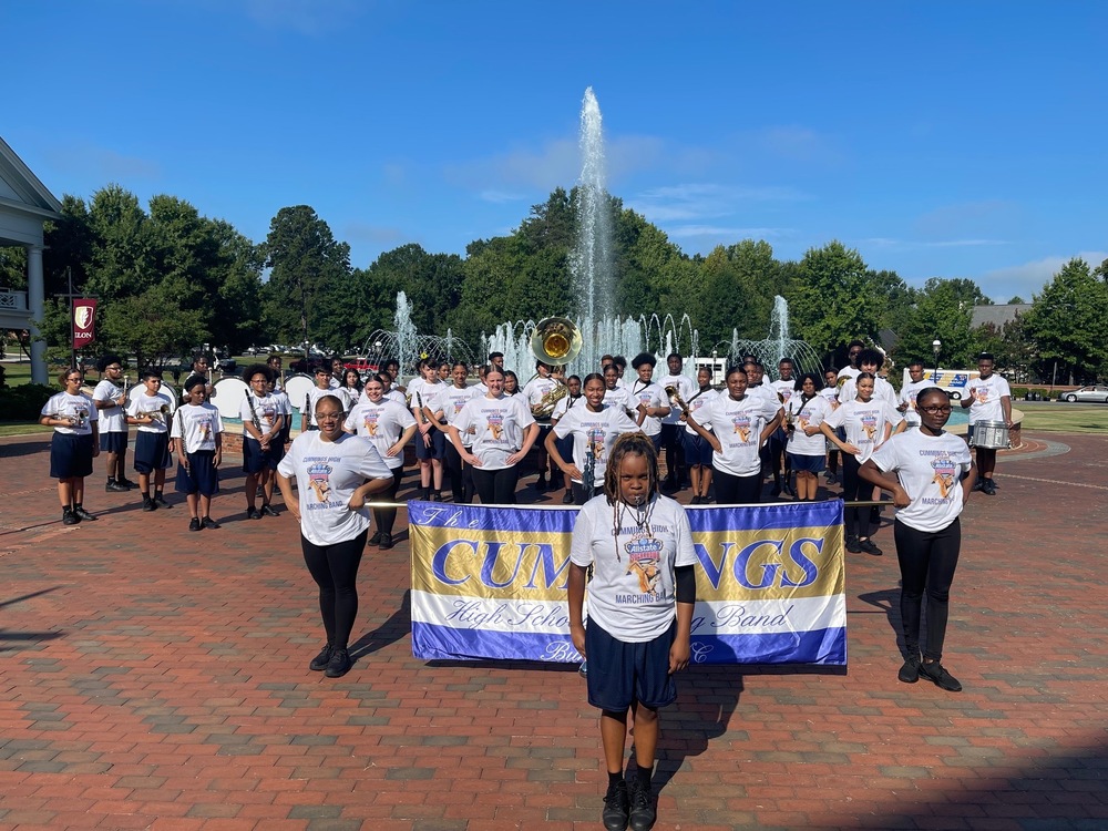 Cummings Band Group photo in front of fountain at Elon University.  Students holding Cummings Band banner 