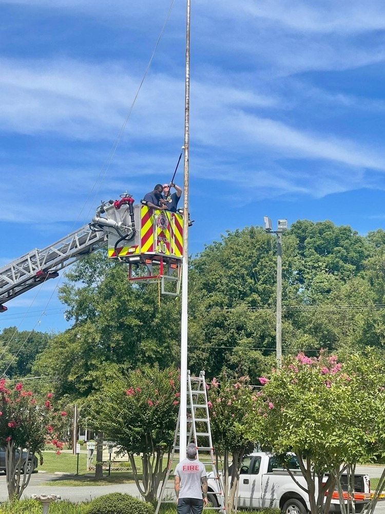 firefighters use ladder truck to paint flagpole at North Graham Elementary