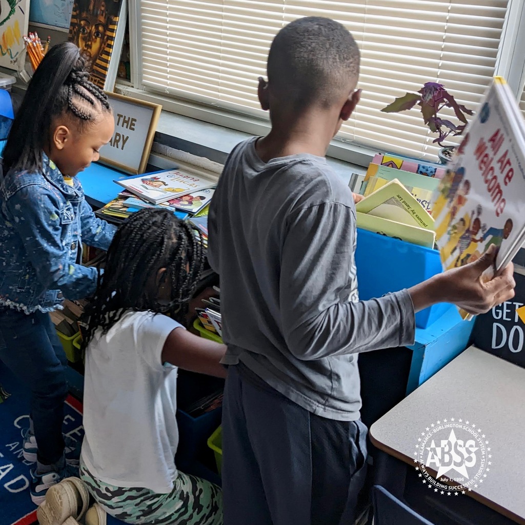 Three young students selecting a book at a blue bookshelf