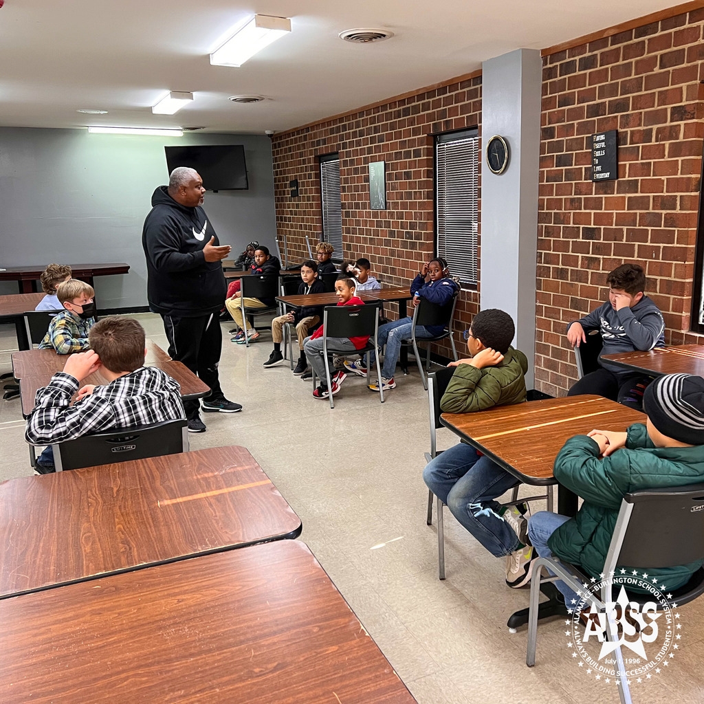 A leader of the Responsible Respectful Boys Group of Pleasant Grove talks to the students sitting at tables inside a homeless shelter