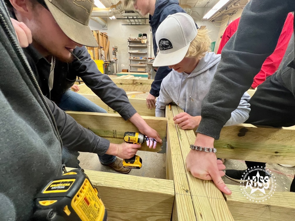 Carpentry students at Eastern Alamance High School working together to create a floor joist for a building foundation using wooden beams.  One student is drilling with a power drill while others hold the beams in place.