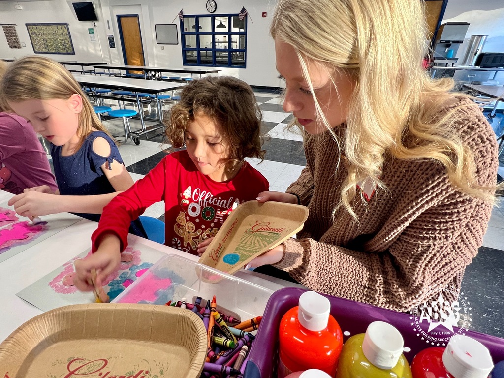 A member of the Southern Alamance High School Student Council assists two elementary girls with a craft project involving paint, crayons, and paper on a cafeteria table