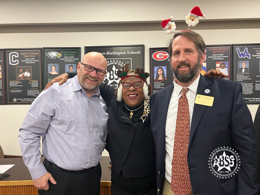 Board of Education members Chuck Marsh, Patsy Simpson, and Dr. Charles Parker standing in the Central Office auditorium.  Chuck Marsh is wearing a festive Santa headband.