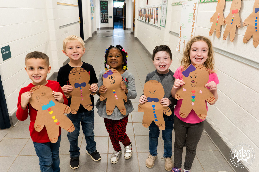 Five students at Andrews Elementary smile and hold large craft gingerbread characters they made