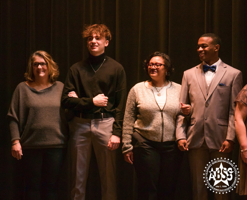 Two Eastern High School students standing in formal wear with members of their family on stage