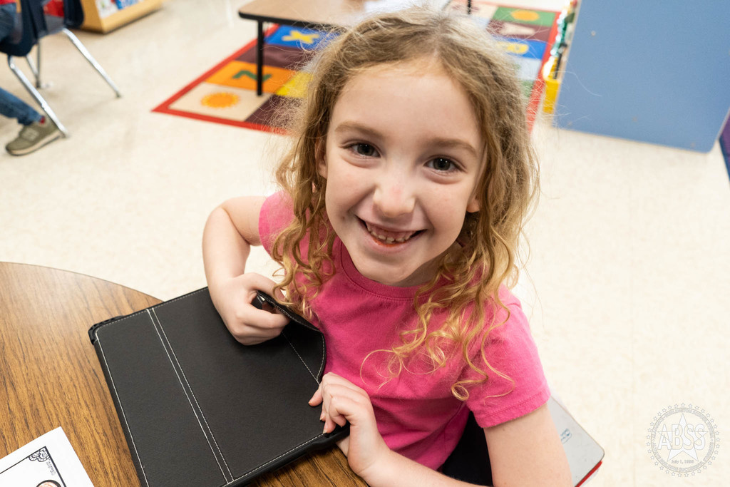 student smiling at camera while sitting at school desk 