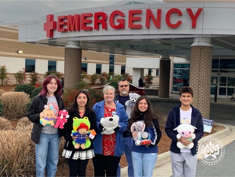students and staff holding stuffed animals in front of the hospital