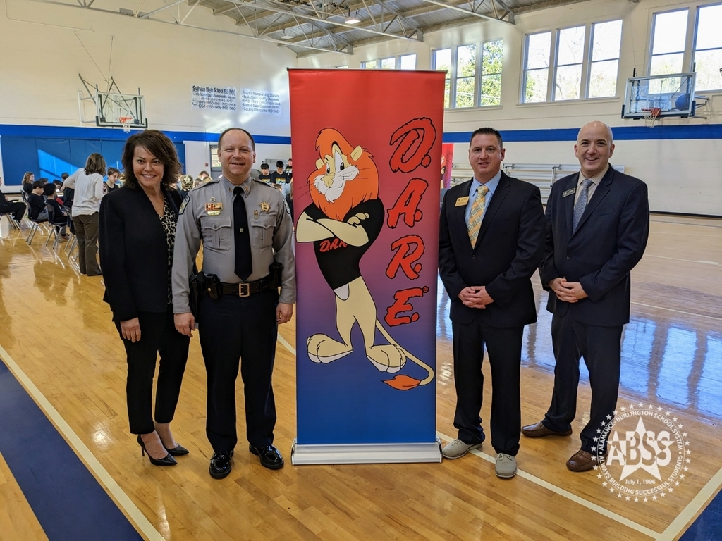 Sergeant Chad law standing with board member Sandy Ellington Graves deputy superintendent lower Rogers and board member Ryan Bowden with a dare poster in the gym at Sylvan elementary