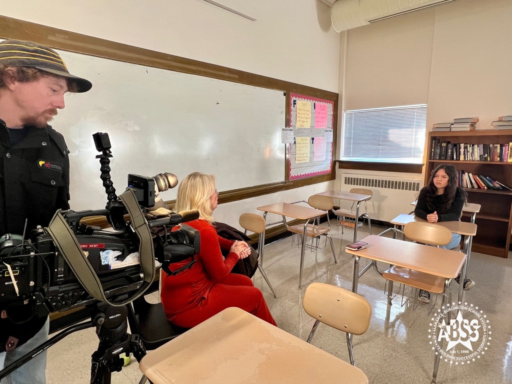 Photograph of Fox 8's Cindy Farmer talking to a Williams High School student in a classroom about their recent donations to children and the homeless.  A cameraman holds a video camera behind Cindy Farmer.
