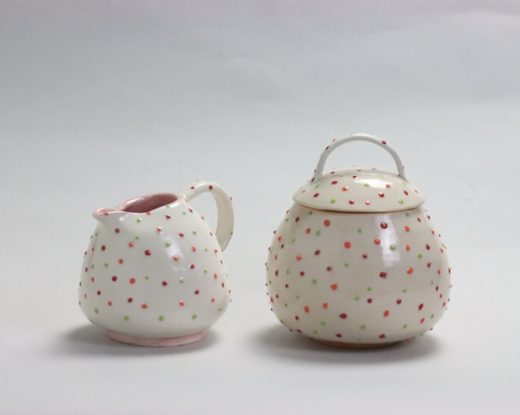 Pottery piece titled:  Valerie Byrd, Grade 12-Honorable Mention "Connect the Dots" .  Two white, glazed teapots are covered in pink, green, and purple dots with a bumpy texture.