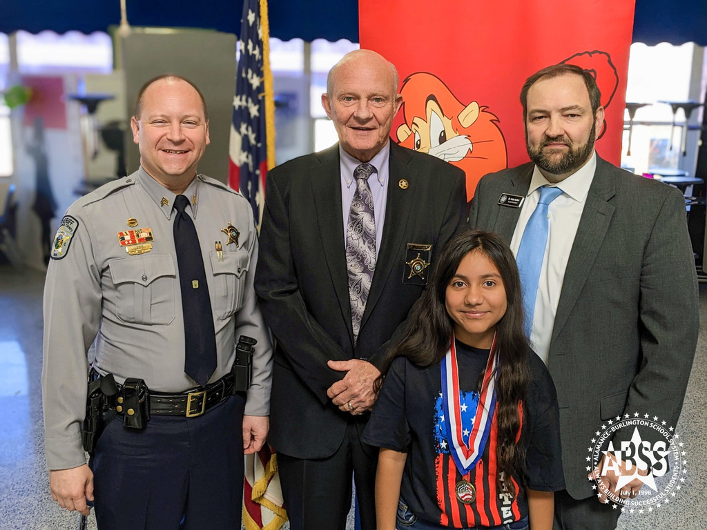 Group photograph of Sgt. Chad Laws, Sheriff Terry Johnson, student Camila Alvarez, and Dr. Butler at the Alexander Wilson DARE graduation