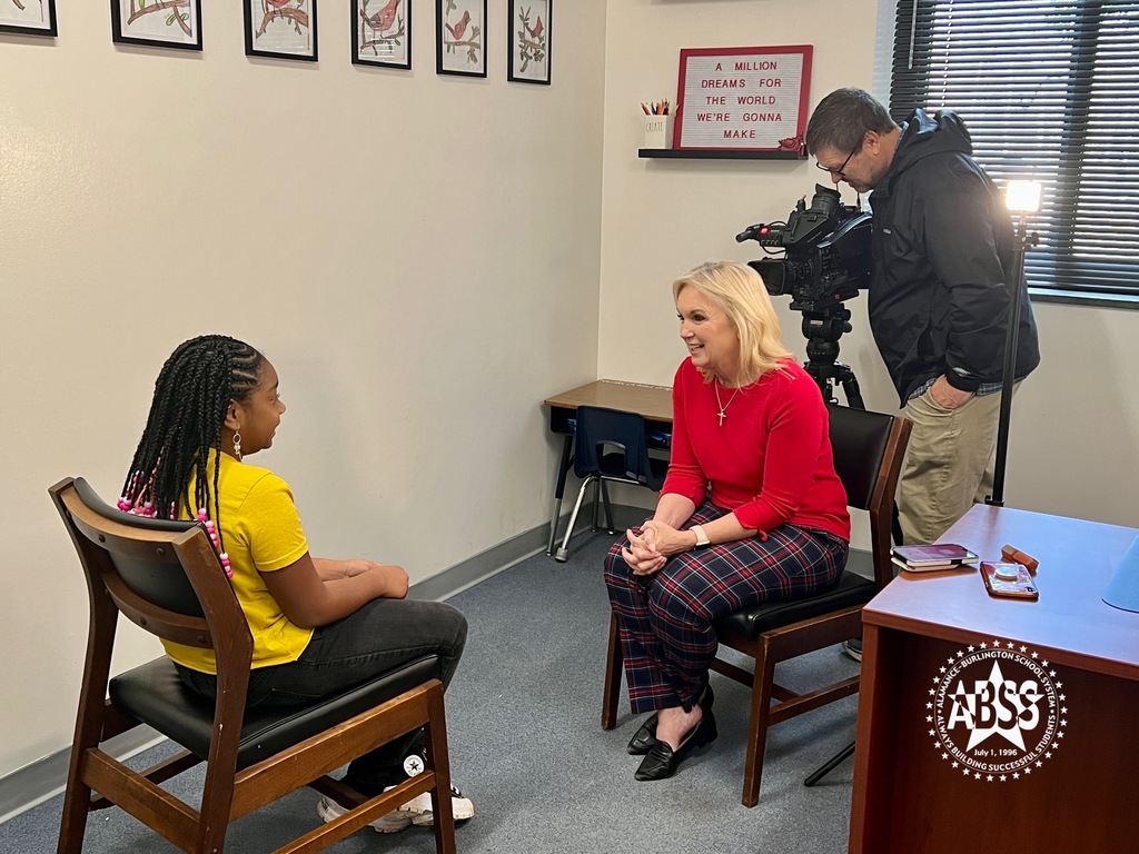 Fox 8's Cindy Farmer interviews a student at North Graham Elementary.  They are both seated in chairs and a camera man is behind Cindy Farmer.
