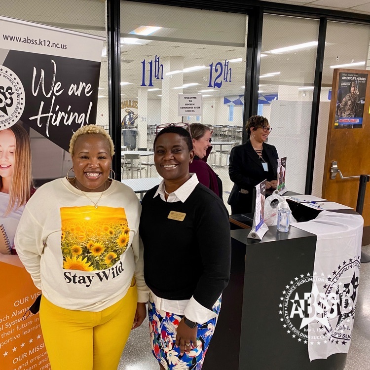 Two staff members in the Alamance Bruns school system, standing in front of an iamb hiring sign at the family university at Cummings high school
