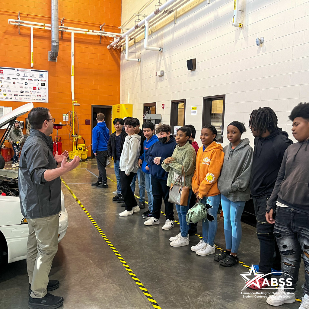 A line of students from Broadview Middle School look on towards an instructor and a vehicle in an automotive classroom at the Career & Technical Education Center