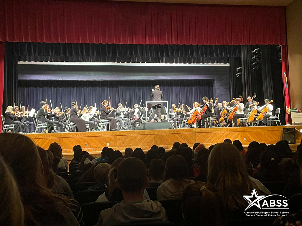 Photograph of the NC Symphony performing on stage for an audience of fourth and fifth grade students and staff