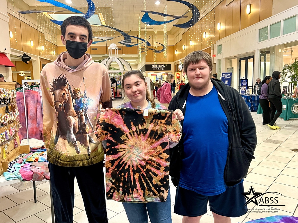 Three students from Western and Williams High School stand beside their both of tie-dye and craft products.  The girl int he middle is holding a tie-dye shirt.