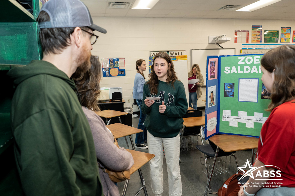 Student at Western Middle School holds a notecard and shares information about Zoe Saldana in front of her presentation board.