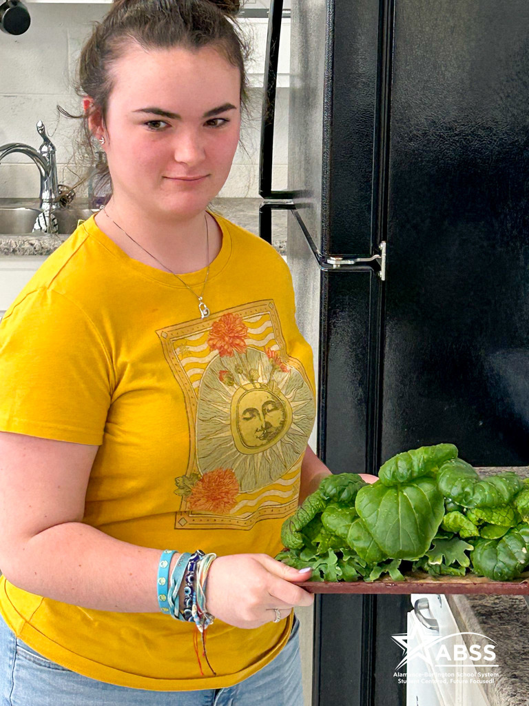 A student carries freshly trimmed and removed greens from a hydroponic garden on a tray