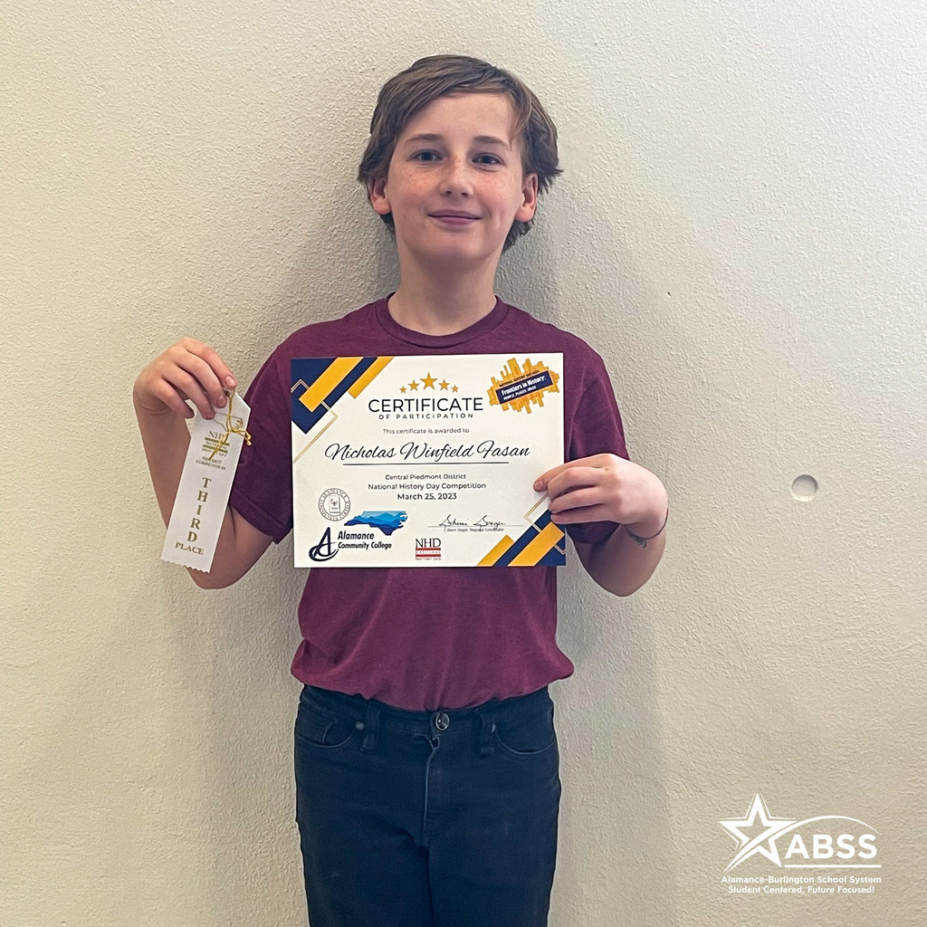 Turrentine Middle School student Nicholas Winfield Fasan wearing a burgundy shirt and dark jeans, holding a ribbon and certificate for his third place recognition in the National History Day paper competition