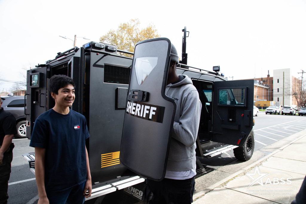 A student holds a bulletproof shield with text SHERIFF on it