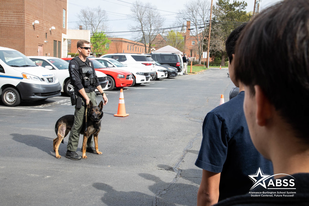 An officer speaks to students while a police dog observes close by