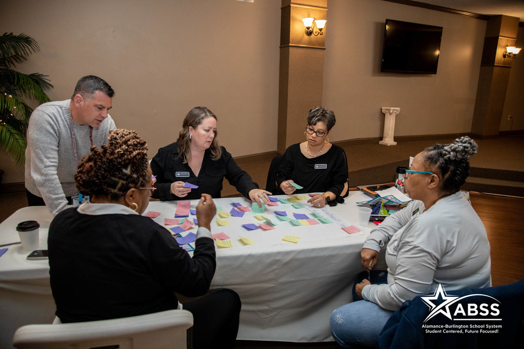 ABSS administrators, staff, and community members analyze sticky notes on a table as part of the Strategic Plan process