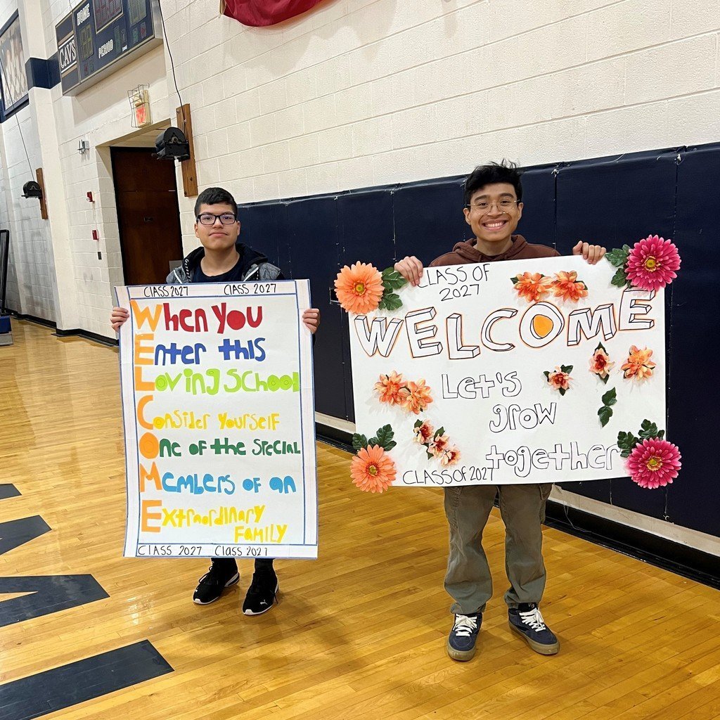 Two high school students hold up motivational signs to rising 9th graders for their high school tour