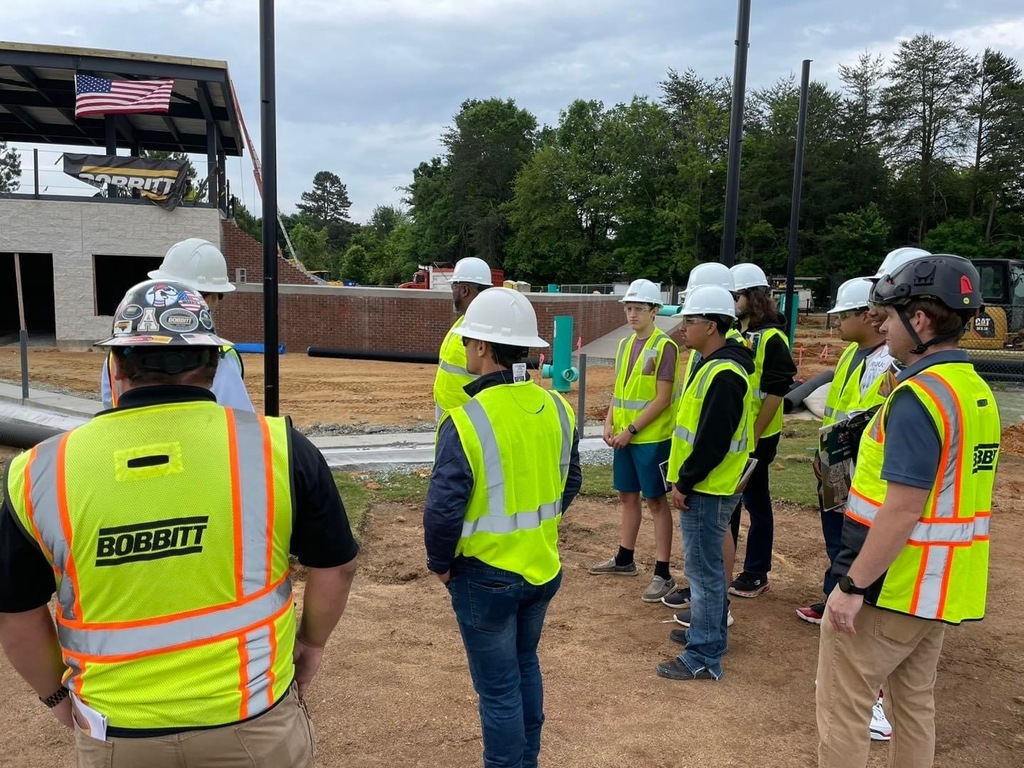 ABSS CTEC students wearing construction vests on a construction site at the Burlington Sock Puppets stadium