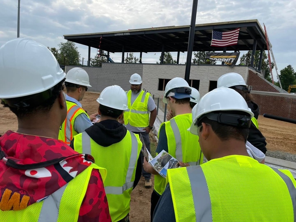 ABSS CTEC students wearing construction vests on a construction site at the Burlington Sock Puppets stadium
