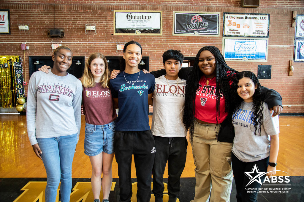 High school seniors at Williams High School standing beside each outer, wearing attire of their chosen college, and smiling at the camera