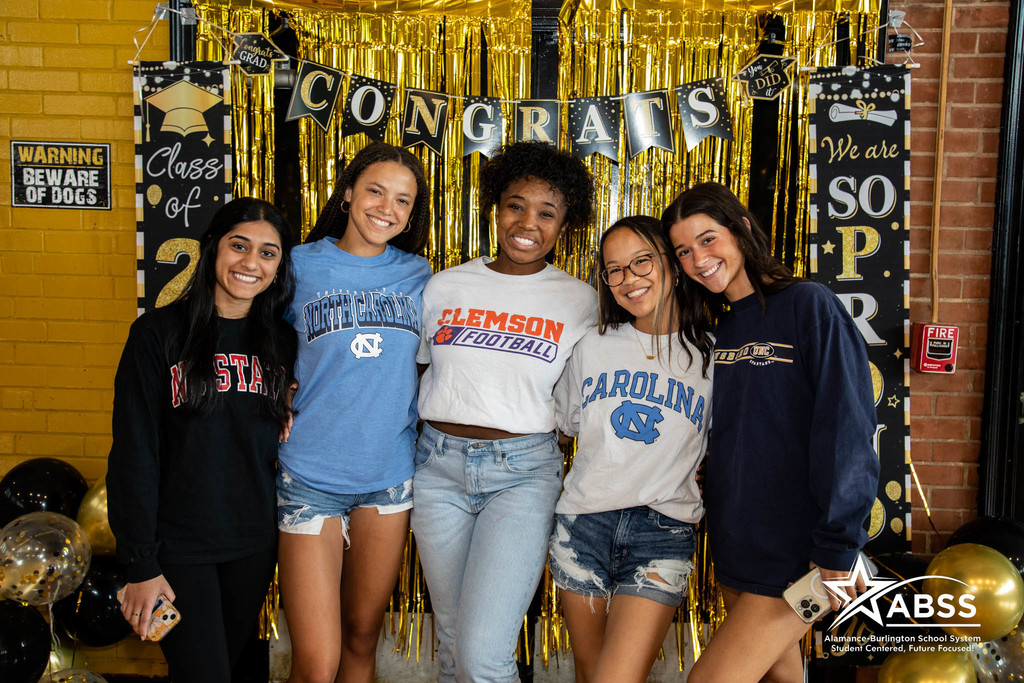 High school seniors at Williams High School standing beside each outer, wearing attire of their chosen college, and smiling at the camera
