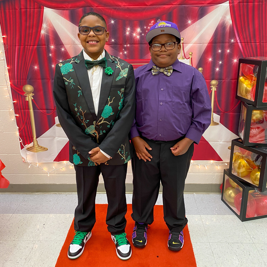 Two students at Hillcrest Elementary dressed in fancy attire in front of a red curtain wall decal and standing on a red carpet