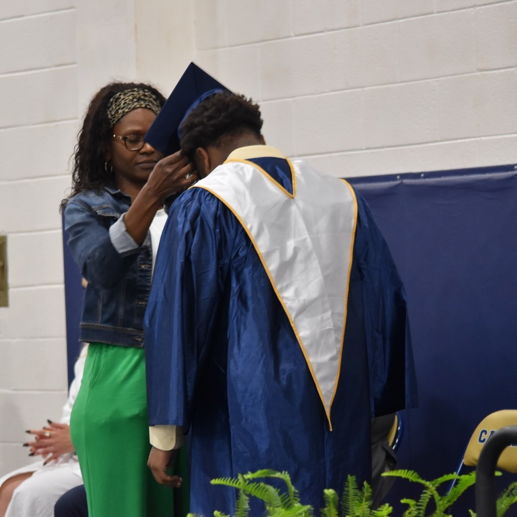 A student has his cap placed on his head by a family figure during the Capping Ceremony at Cummings High School