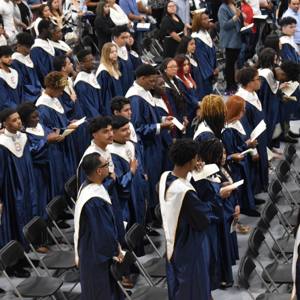 Group photograph of seniors standing in front of rows of chairs wearing their graduation gowns