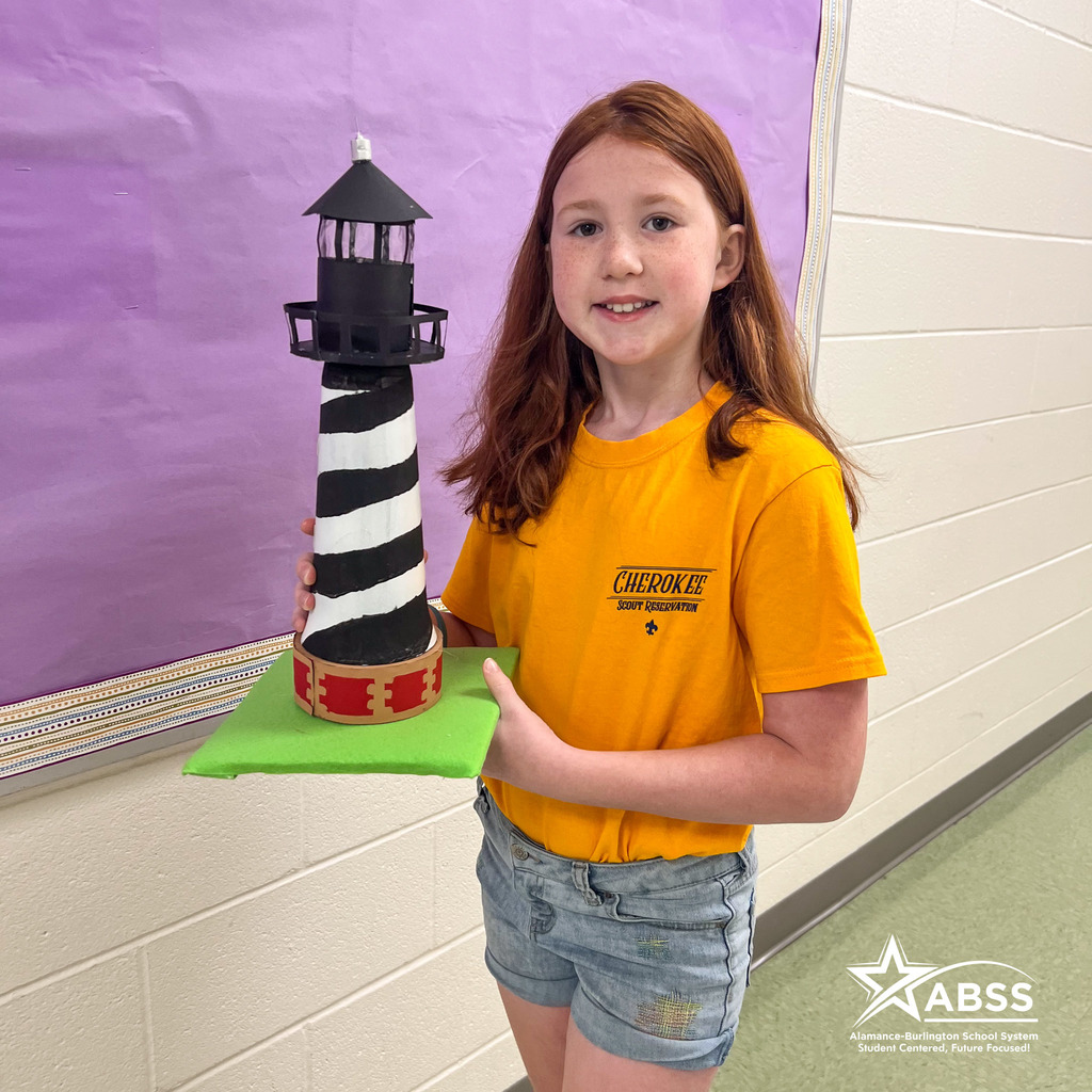 An Elon Elementary fifth grader wearing a yellow shirt holds a model of Cape Hatteras lighthouse she created for a project