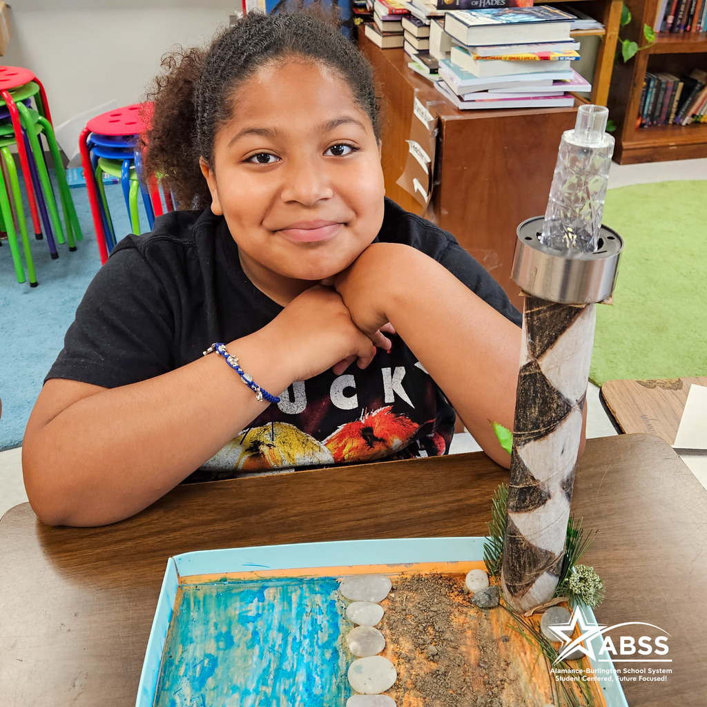 An Elon Elementary fourth grader sits beside a model of Cape Lookout lighthouse she created for a project