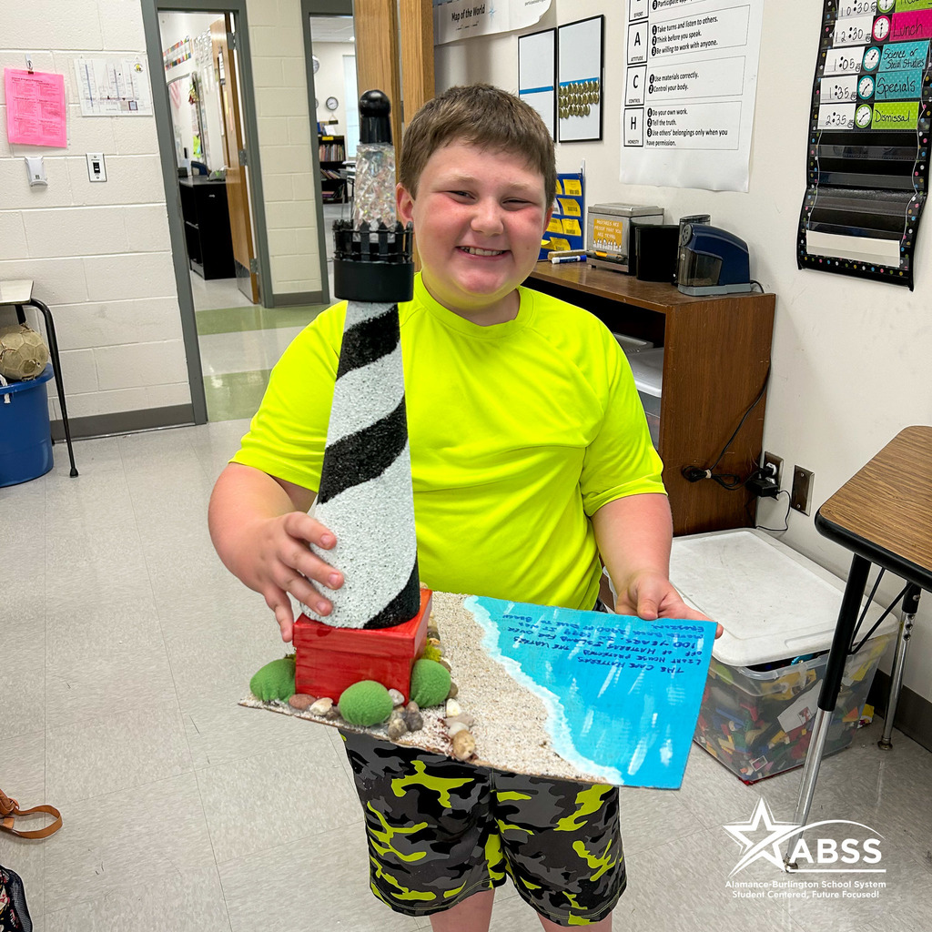 An Elon Elementary fourth grader stands and holds a scale model of Cape Hatteras lighthouse he created using foam, paint, seashells, and other materials