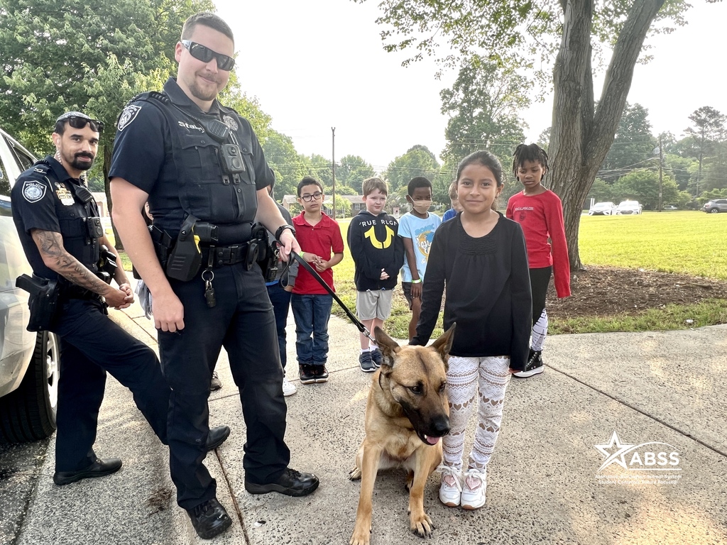 Students at Newlin Elementary standing with Burlington Police Department officers and a police dog on a leash