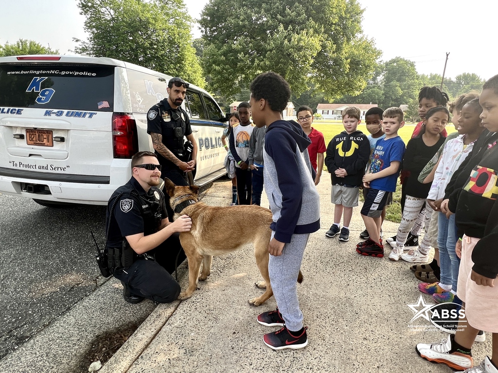 Students at Newlin Elementary interacting with Burlington Police Department officers and a police dog on a leash
