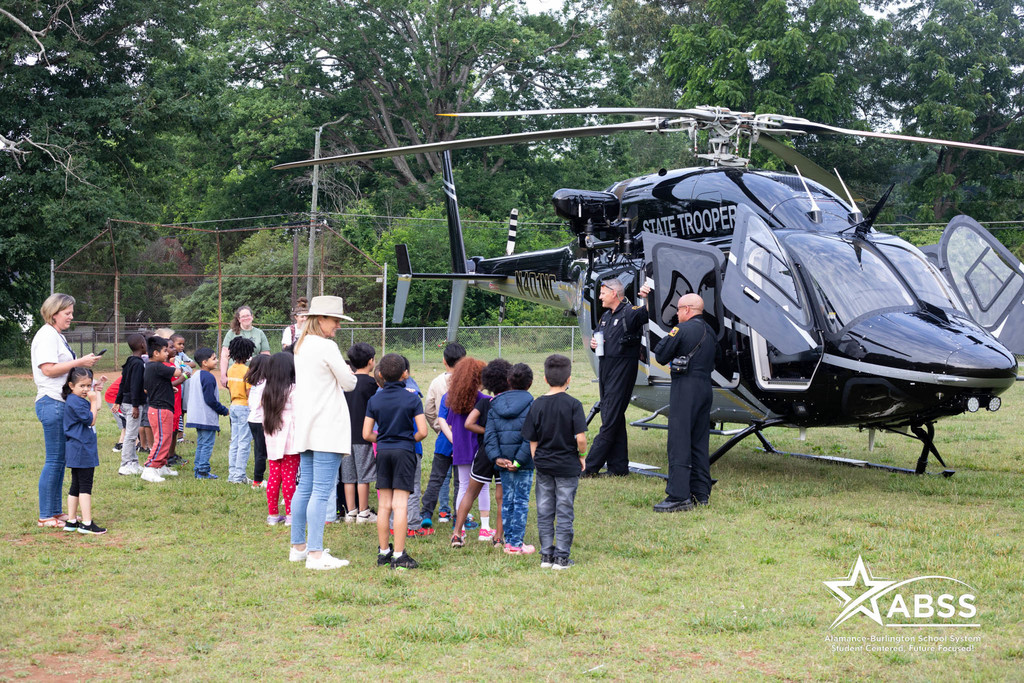 NC Highway Patrol officers stand in front of a helicopter with a group of Newlin Elementary students in front listening 