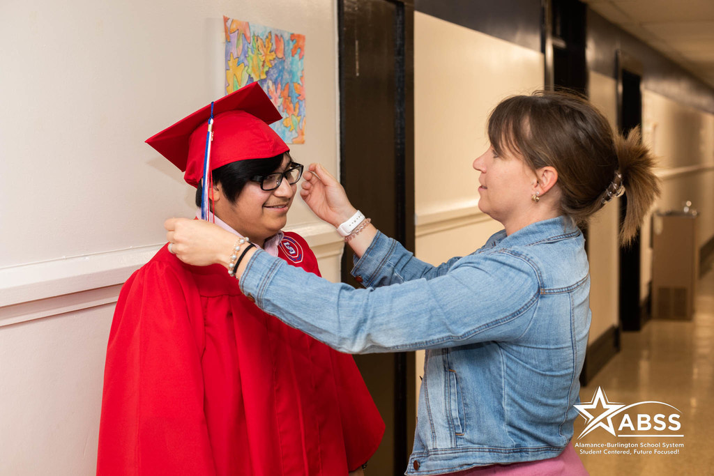 A graduate of Ray Street Academy in red robes has his tassle adjusted by a staff member