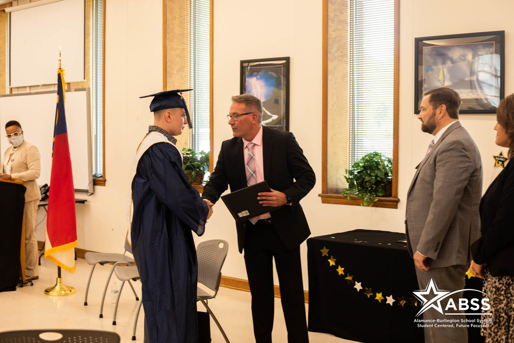 Principal Bayless shakes the hand of a graduate in blue robes of Ray Street Academy 