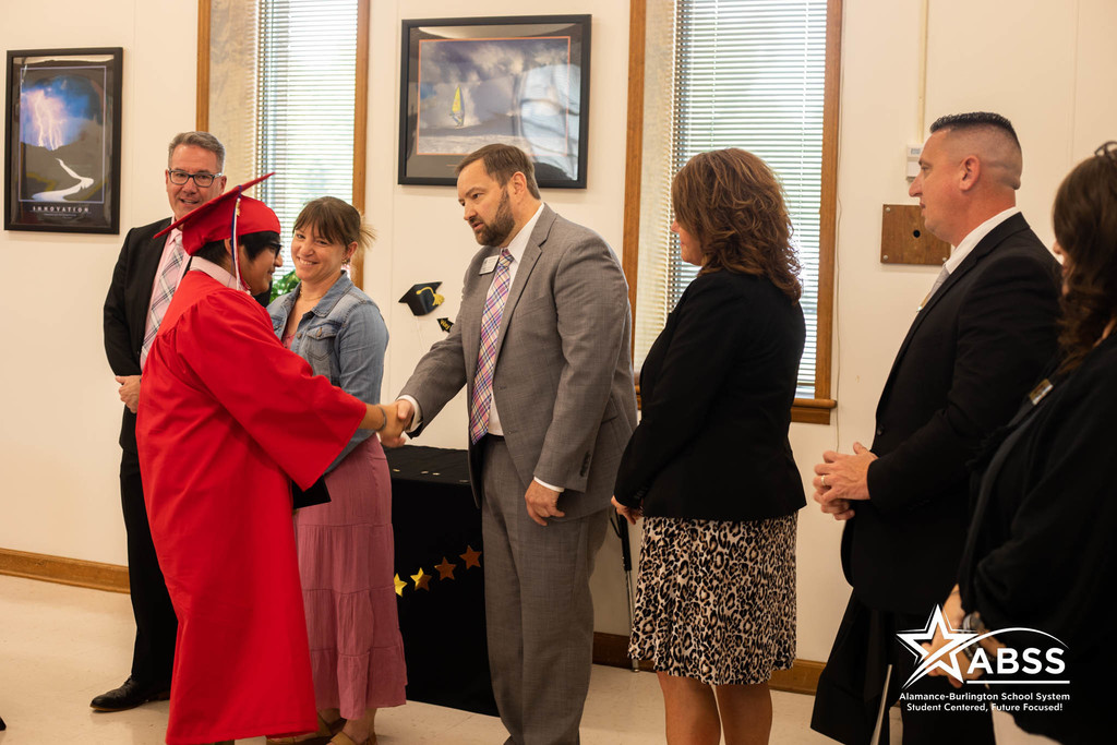Superintendent Dr. Dain Butler shakes the hand of a graduate in red robes at Ray Street Academy