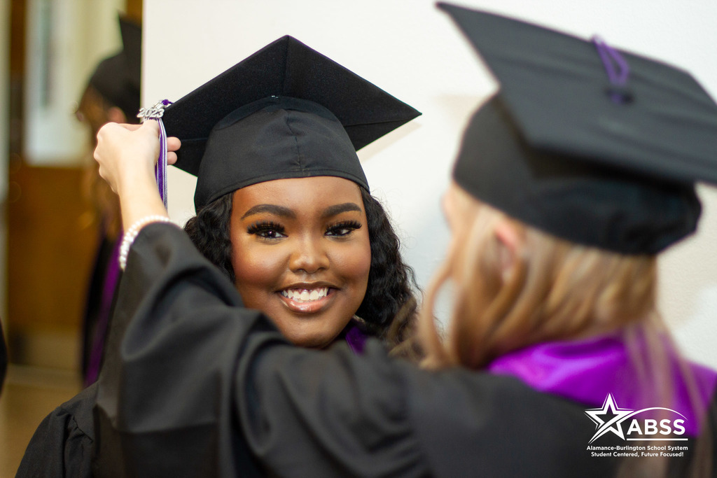A girl wearing a graduation cap has her tassel adjusted by another student at the Alamance virtual School graduation ceremony