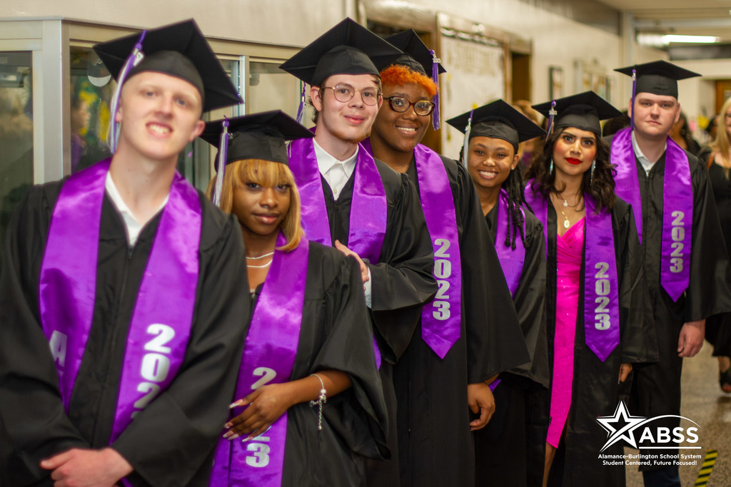 A row of Alamance Virtual School seniors in cap and gowns smiling at the camera