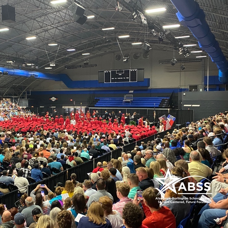 Graduation ceremony at Greensboro Coliseum Fieldhouse with full seats of graduates, staff, and families 