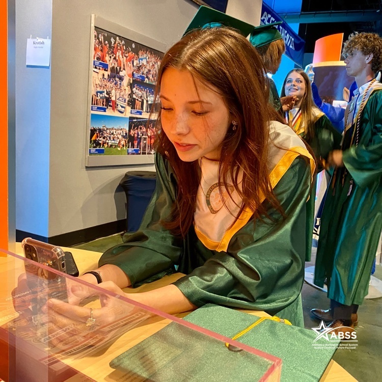 A graduate of Eastern High School in her robes looks at her phone as she takes a selfie